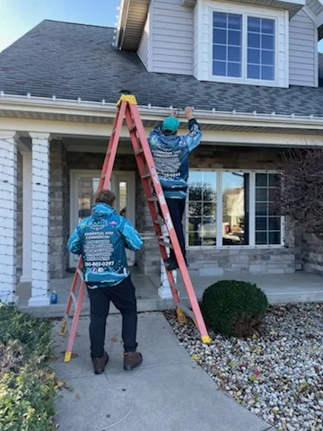 Elite crew member on a ladder installing Christmas lights on a roofline